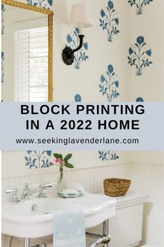 a white sink sitting under a bathroom mirror next to a wallpapered wall with blue flowers on it