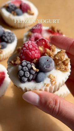 a person is holding up some fruit and yogurt bites with granola on top