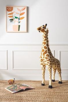 a stuffed giraffe standing next to a book in a room with white walls