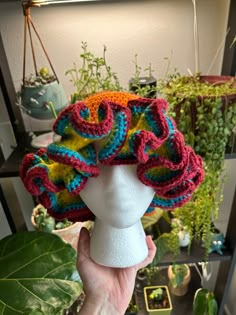 a person holding up a crocheted hat on top of a mannequin head