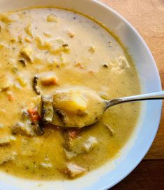 a white bowl filled with soup sitting on top of a wooden table next to a spoon