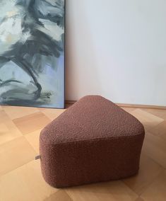 a large brown ottoman sitting on top of a hard wood floor next to a painting