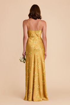 the back of a woman wearing a gold dress with flowers on it and her hands in her pockets