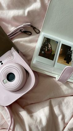 a pink camera sitting on top of a bed next to an open book and photo album