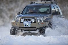 a jeep driving through the snow with its lights on and front bumper mounted to it