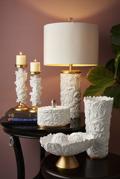 a table topped with two white vases next to a lamp and a candle holder