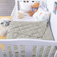 a white crib with a teddy bear on the bed next to pillows and blankets