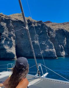 a woman sitting on top of a boat in the ocean next to a rocky cliff