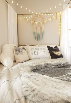 a white bed topped with lots of pillows next to a window covered in string lights