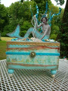 a statue of a mermaid sitting on top of a chest with pearls in her hair