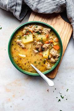 a bowl of soup with meat, potatoes and carrots on a wooden cutting board