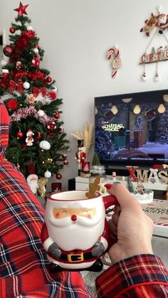 a person holding a coffee cup in front of a christmas tree and television set with decorations on it