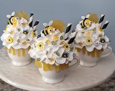 three small vases with flowers and bees in them sitting on a marble counter top