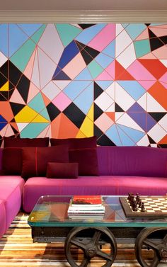 a living room filled with furniture and a colorful wall behind the couch is a glass coffee table