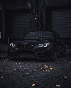 a black sports car parked in front of garage doors at night with leaves on the ground