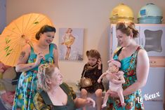 three women and two children are in a room with umbrellas on the wall, one is holding a doll