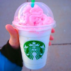 a person holding up a starbucks drink with pink ice cream on the top and green straw sticking out of it