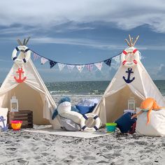 two teepee tents on the beach with pillows and toys in front of them,