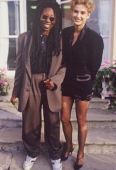 two women standing next to each other in front of a building with flowers on the steps