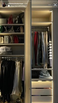 an open closet with clothes and handbags hanging on the shelves, in front of a mirror