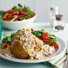 a white plate topped with salad next to a bowl filled with vegetables and bread on top of a table