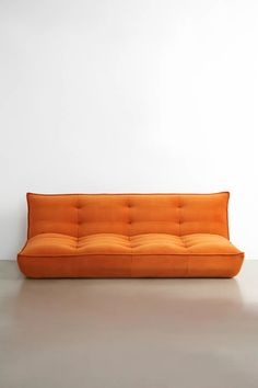 an orange couch sitting on top of a white floor next to a wall and chair