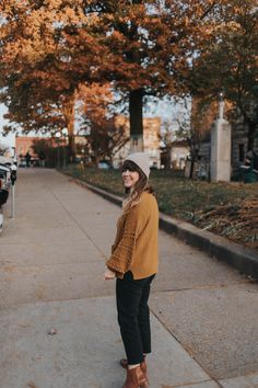 a woman is standing on the sidewalk in front of some trees and wearing a hat