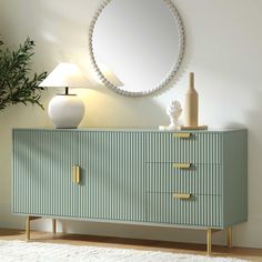 a green and white dresser with a round mirror above it on the wall next to a lamp