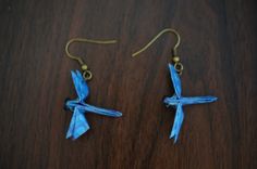 two small blue birds are hanging from gold earwires on a wooden surface,