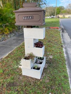 a mailbox sitting in the grass next to a planter with plants growing out of it