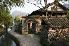 an old stone building next to a river with trees on both sides and mountains in the background