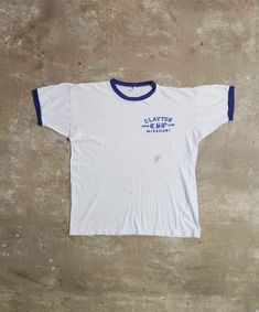 Take a closer look at this unique vintage 1970s Champion Clayton Missouri Swim Team ringer tee. Its authentic design and history make it a must-have for vintage enthusiasts and a perfect addition to your summer wardrobe. Measurements: Pit-Pit: 21.5" Length: 25" This tee has been well-loved, showing signs of its age with discoloration throughout and a repair on the side front area. Please see all the pics for a detailed view of the wear and tear.  This item may have flaws due to its vintage nature. Any major flaws will be recorded. Please anticipate imperfections, as these items are recycled vintage. Vintage Raglan Tee, White Vintage Top With Vintage Print, Vintage Cropped T-shirt For Summer, Vintage White Cotton T-shirt, Vintage White T-shirt With Screen Print, Vintage Screen Print Tops, Clayton Missouri, Ringer Tee Vintage, Wardrobe Measurements