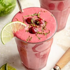 two glasses filled with smoothie and garnished with cherries next to watermelon wedges