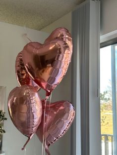 some pink heart shaped balloons hanging from a window sill in front of a white wall