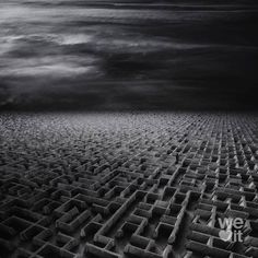 an abstract black and white photo of a maze in the sand with dark clouds above