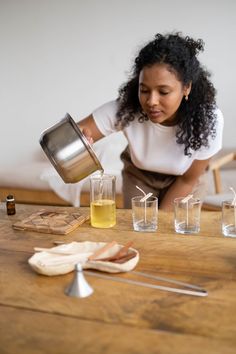 a woman pours some liquid from a pitcher into glasses on a table with other items