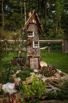 a tree house made out of rocks in the middle of a yard with flowers and plants around it