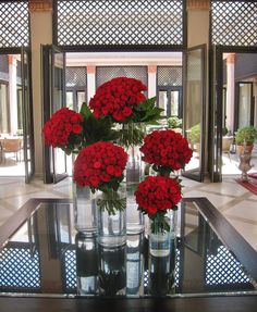 four vases filled with red flowers sitting on top of a glass table in front of an open door