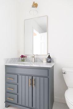 a white toilet sitting next to a gray vanity with a mirror on it's side