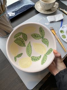 a person is holding a bowl with lemons painted on it and paintbrushes next to the bowl