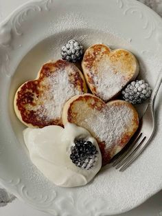 heart shaped pancakes with powdered sugar and blackberries on a white plate next to a fork