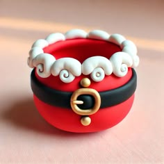 a red and black ring with white beads on it sitting on a pink surface next to a pair of scissors