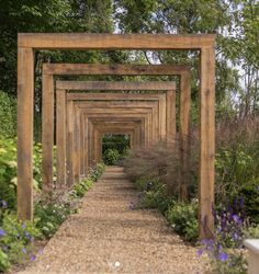 a wooden arch in the middle of a garden filled with purple flowers and greenery