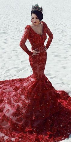 a woman in a red dress standing on the beach wearing a tiara and holding her hands on her hips