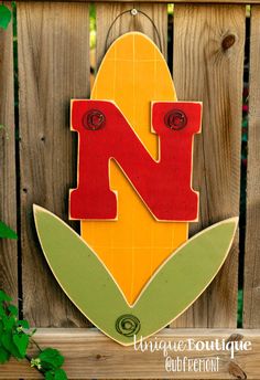 a wooden sign with the letter n painted on it's side and leaves surrounding it