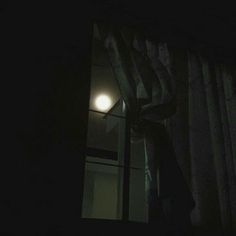 a person standing in front of a window at night with the light on and curtain pulled down