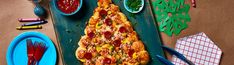 a pizza sitting on top of a green tray next to paper plates and utensils