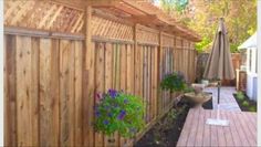 a wooden fence next to a yard with flowers and an umbrella on top of it