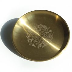 a gold plate with designs on it sitting on a white table top next to a shadow