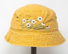 a yellow hat with daisies on it sitting on top of a wooden stand next to a white wall